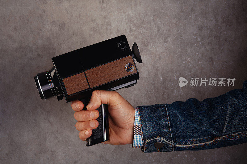 摄像机操作员拿着老式模拟Super8, 8毫米电影摄像机在混凝土墙前。把相机对准枪